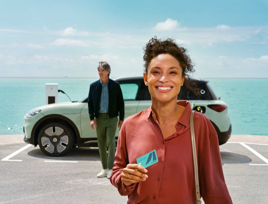 A driver beside an electric car, phone in hand